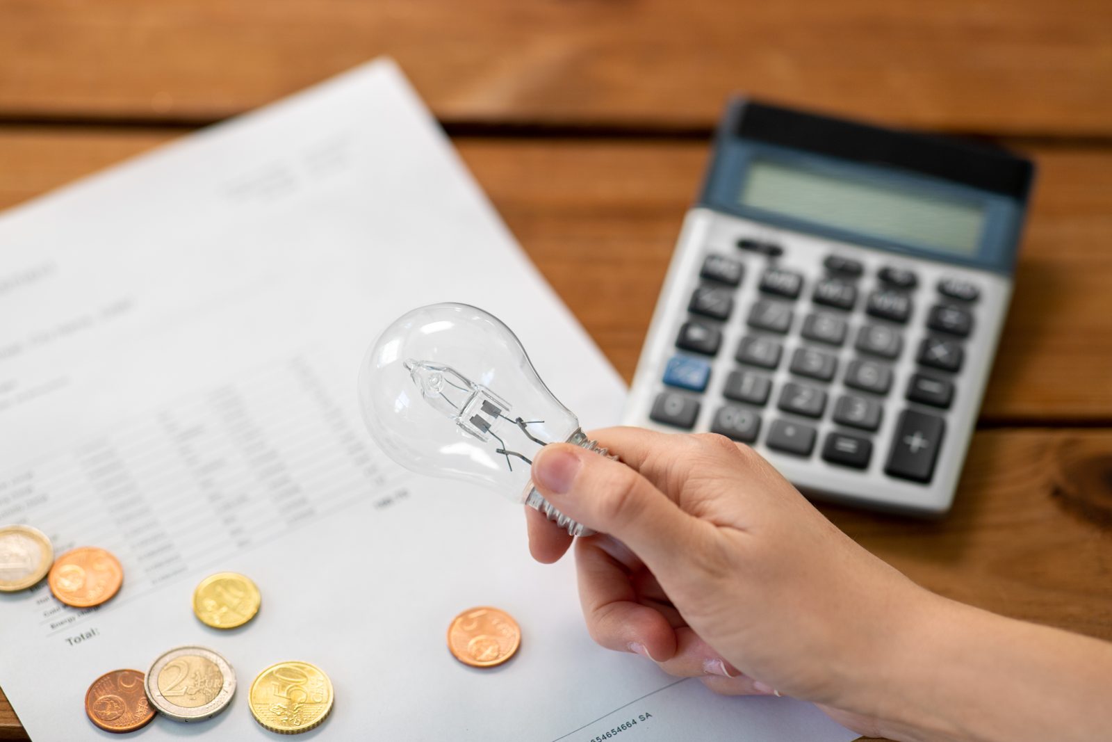 Por qué sube la luz: bombilla, monedas y calculadora sobre una factura de electricidad